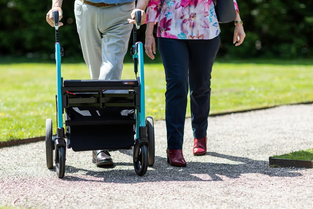 pexels-photo-19971191-19971191 Elderly couple walking together with a walker on a sunny day in a park.
