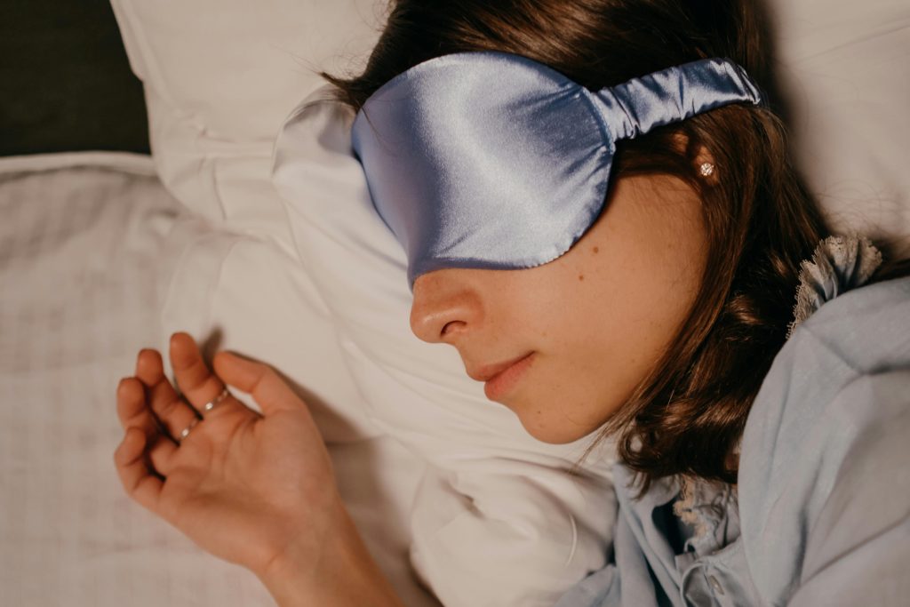 A woman wearing a silk eye mask sleeping peacefully on a pillow.