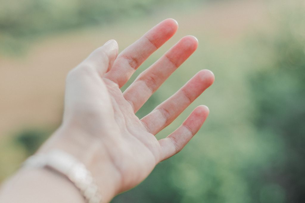 A close-up of an outstretched hand in soft focus with a blurred natural background.
