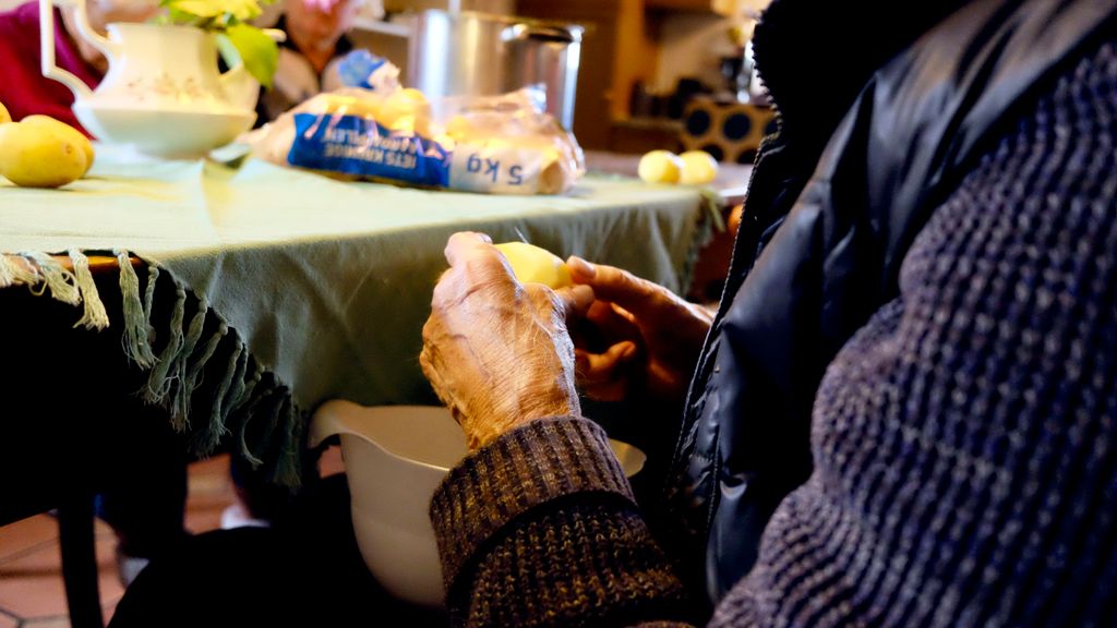 A senior adult peels potatoes at a kitchen table, showcasing culinary routine.