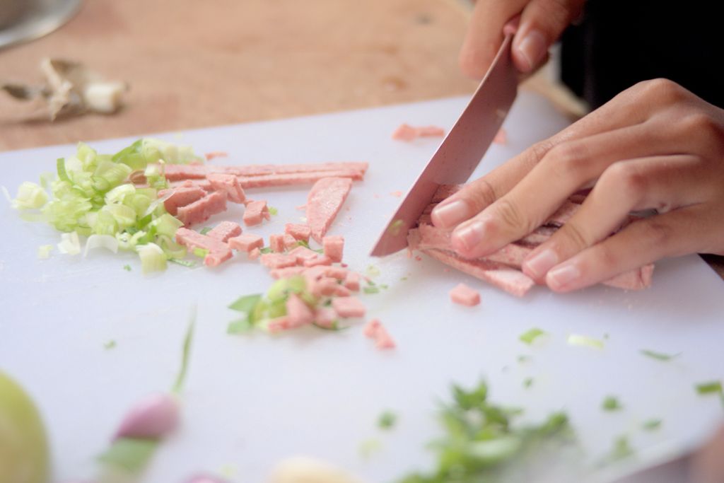 Hands cutting ham and scallions on a cutting board for a fresh meal prep.