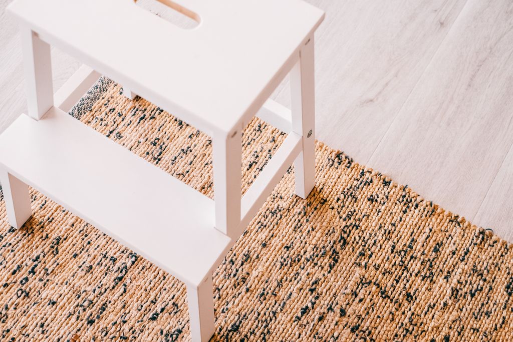A clean, minimalist stepladder on a natural woven rug in a stylish interior.
