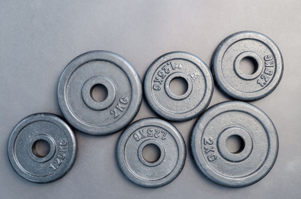 Close-up of steel gym weight plates in various sizes arranged on a gray surface.