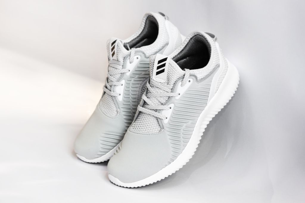 Pair of sports shoes with gray dense texture of surface and rubber inserts from sided and laces and white soles placed with heels up leaning on glance gray background